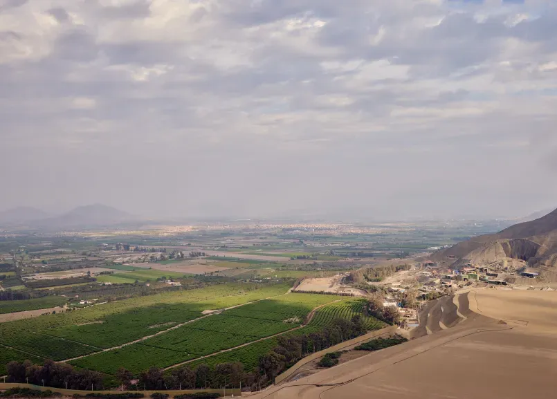 Dos colaboradores en la obra, uno con chaleco naranja y el otro con chaleco verde neón, revisando documentos junto a un equipo topográfico.