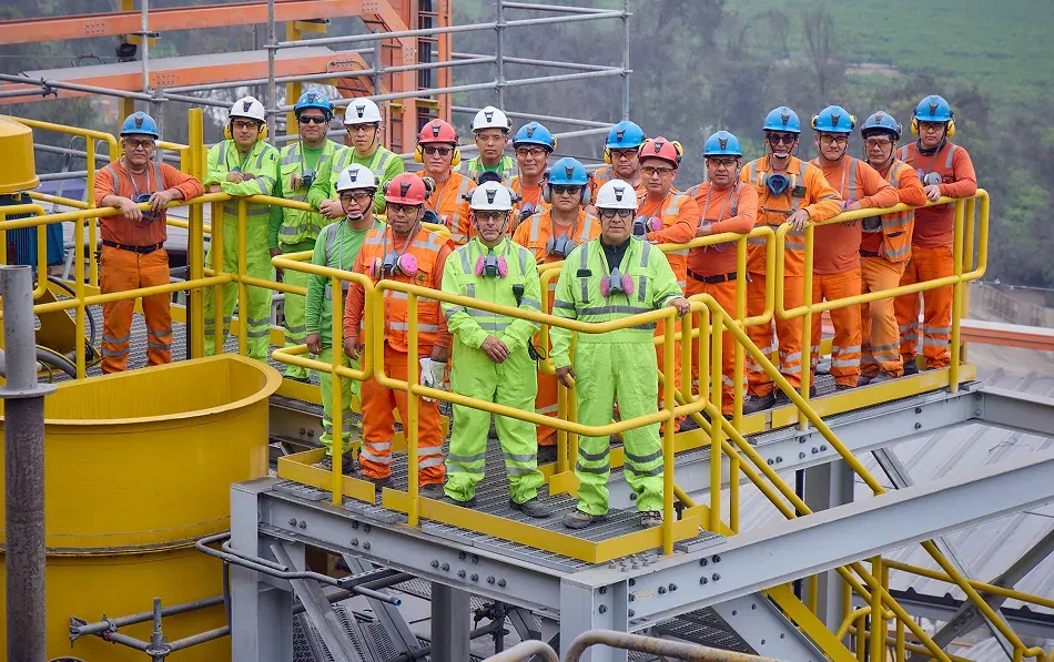 Grupo de niños o jóvenes con cascos de seguridad blancos y chalecos verde neón, prestando atención.